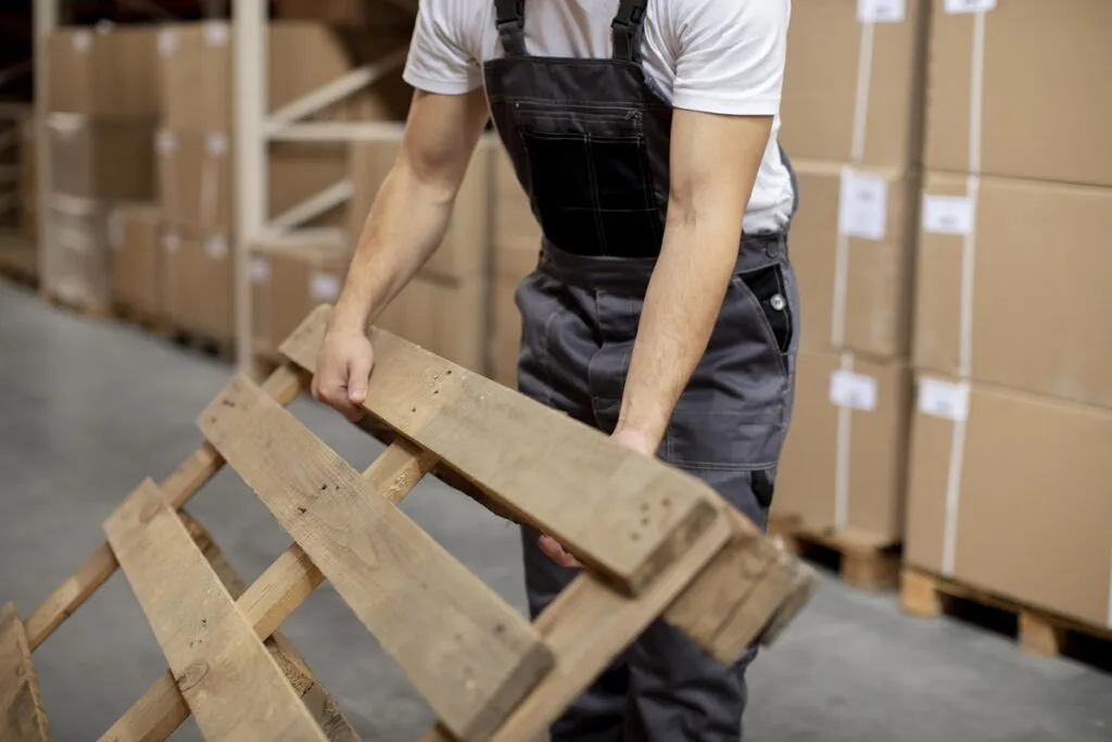 Homem carregando um pallet de madeira.